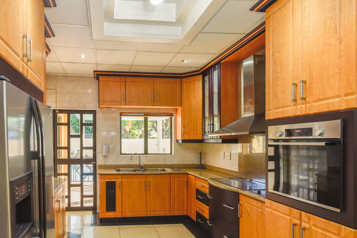 A functional kitchen featuring wooden cabinetry, granite countertops, a built-in oven, stainless steel extractor fan, and a double sink with garden access.