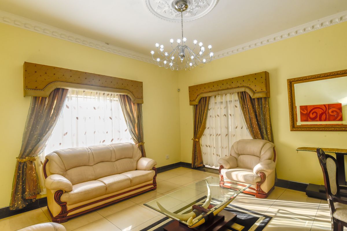 A formal living room featuring decorative ceiling cornicing, a central chandelier, and large windows with built-in pelmets.