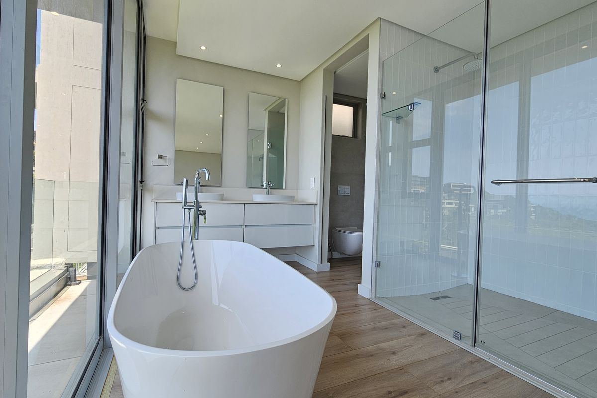 Modern bathroom featuring a freestanding bathtub, glass-enclosed walk-in shower, double vanity with vessel sinks, and large windows offering natural light.