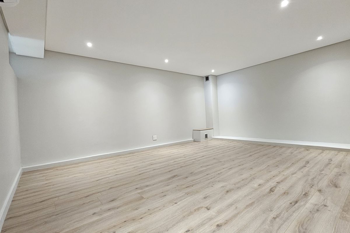 A bright, spacious, and empty living area featuring modern light wood-look laminate flooring, recessed downlighting, and clean, neutral wall finishes.