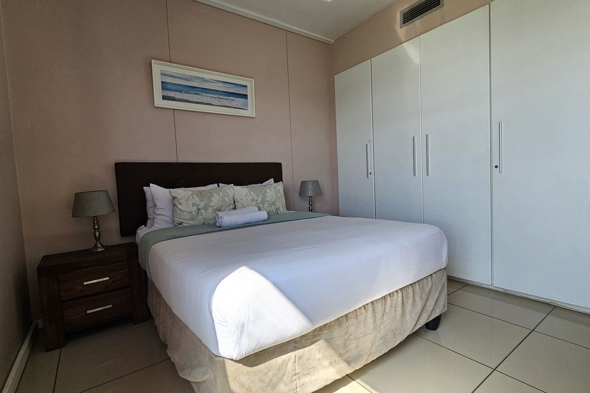 A bedroom featuring built-in white floor-to-ceiling wardrobes, tiled flooring, and ducted air conditioning vents.