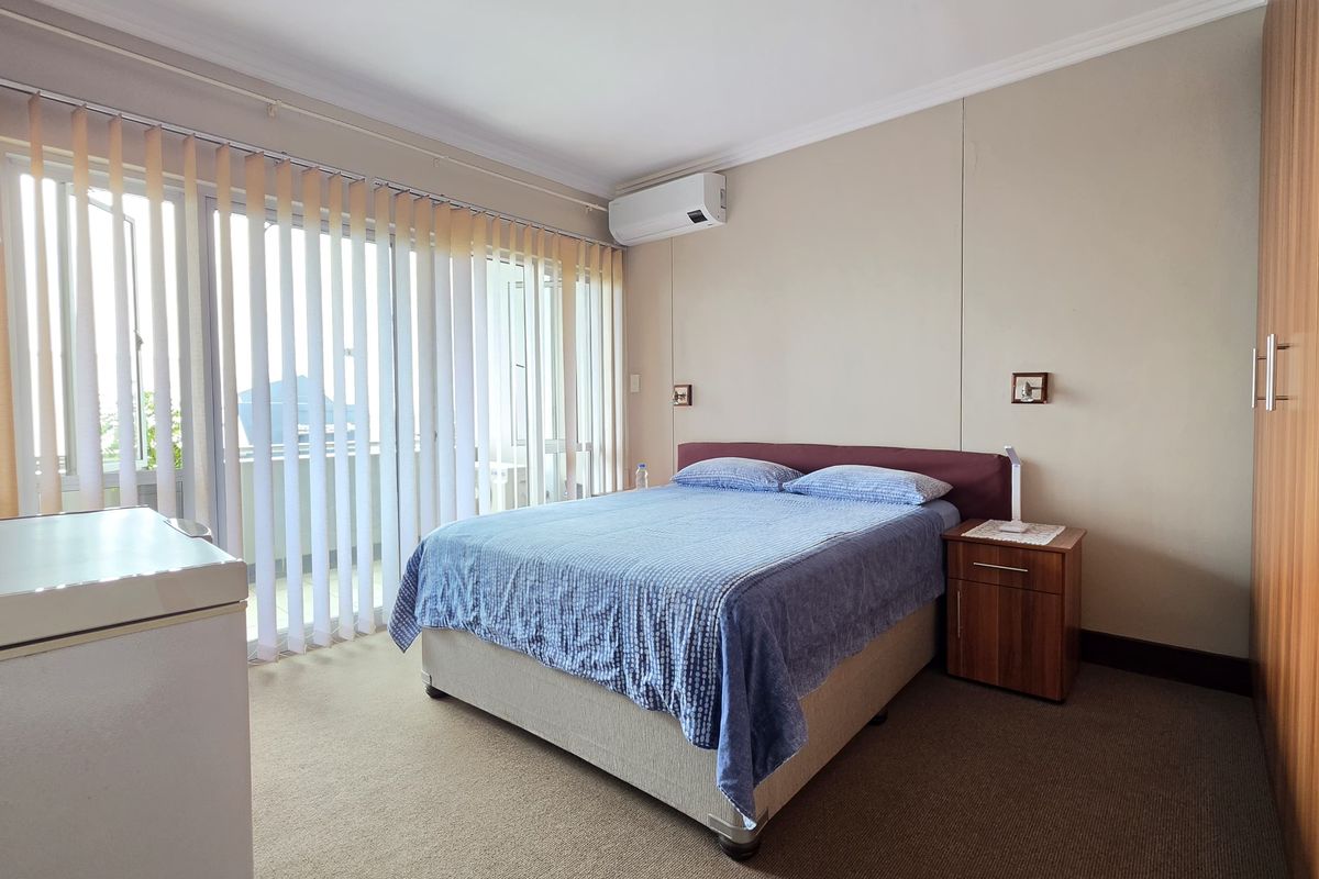 A bedroom featuring built-in wooden wardrobes, wall-mounted air conditioning unit, and large sliding glass doors leading to a balcony.