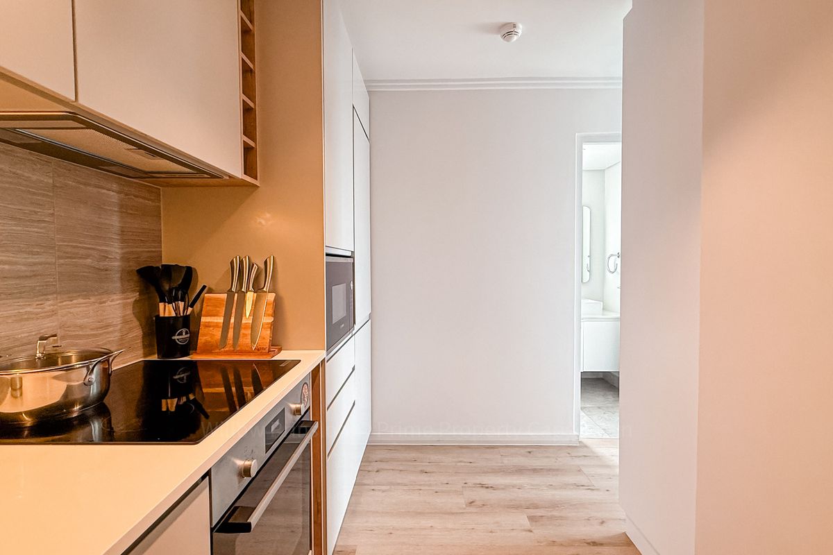 Modern kitchen featuring integrated oven, induction hob, extractor fan, and sleek cabinetry with wood-look flooring, leading to an adjacent bathroom.