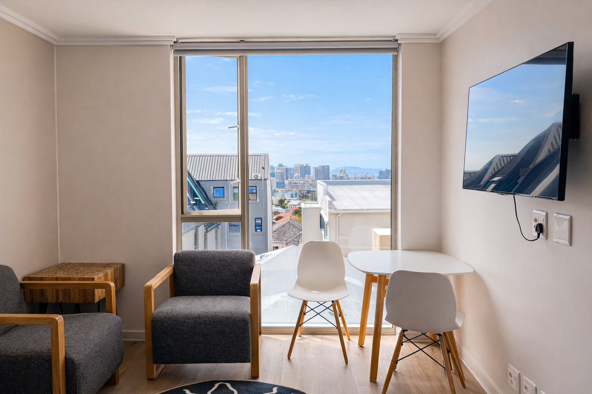 A bright living area featuring large windows with expansive city views, neutral wall finishes, and integrated wall-mounted television connectivity.