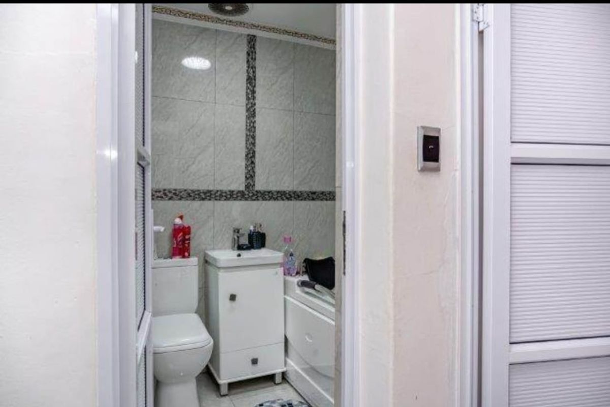 A compact bathroom featuring tiled walls, a pedestal vanity, a toilet, and a bathtub, viewed through a doorway.