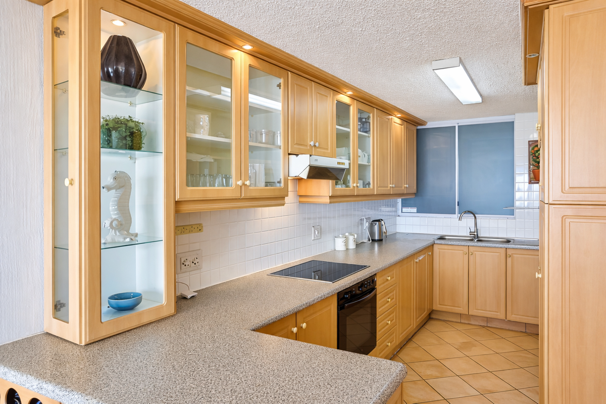 A functional kitchen featuring light wood cabinetry, a built-in oven, electric hob, extractor fan, and tiled backsplash with ample counter space.