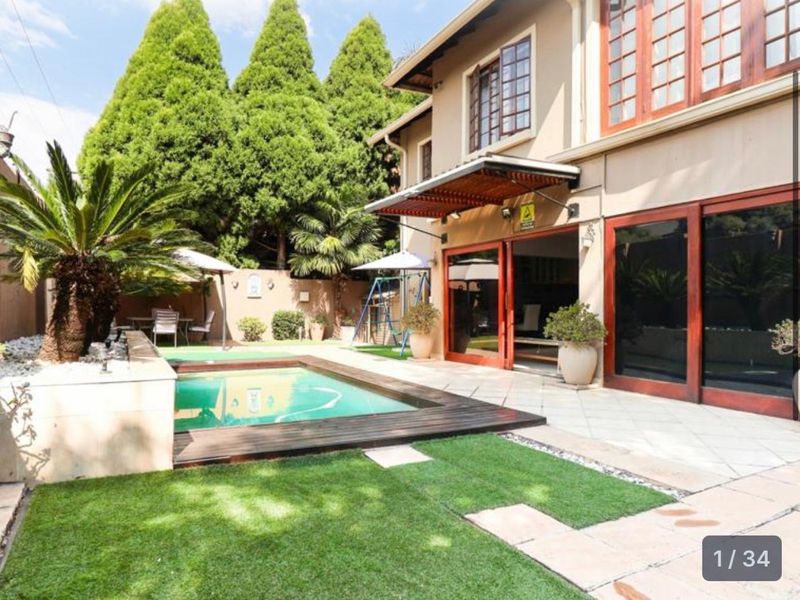 A well-maintained outdoor pool area featuring a swimming pool with timber decking, a tiled patio, and direct access to the home via sliding doors.
