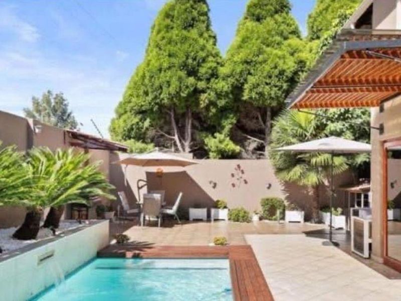 A well-maintained outdoor entertainment area featuring a swimming pool, tiled patio, and a timber pergola, enclosed by a private boundary wall.