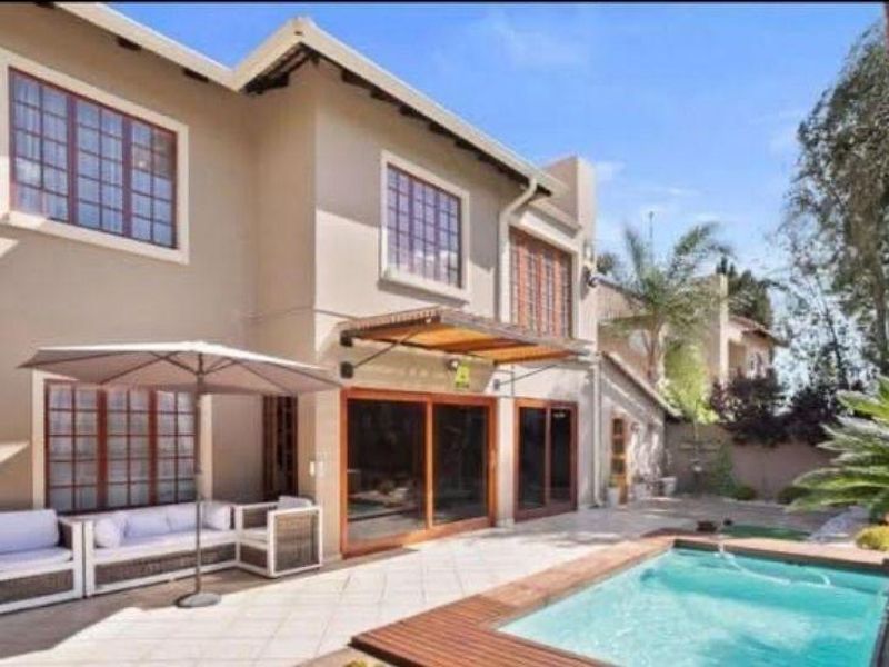 Rear exterior view featuring a tiled patio, swimming pool with wooden decking, and large sliding glass doors leading into the home.