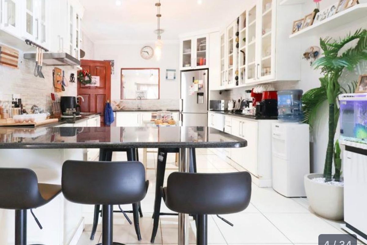 A bright, well-maintained kitchen featuring white cabinetry, granite countertops, a central breakfast bar, and tiled flooring with ample storage space.