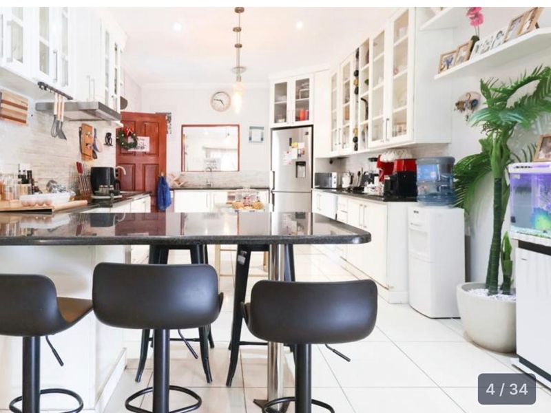 A bright, well-maintained kitchen featuring white cabinetry, granite countertops, a central breakfast bar, and tiled flooring with ample storage space.