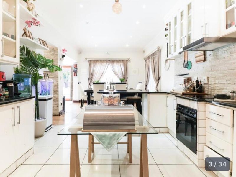 Open-plan kitchen and dining area featuring white cabinetry, stone cladding accents, and tiled flooring, creating a bright and functional living space.