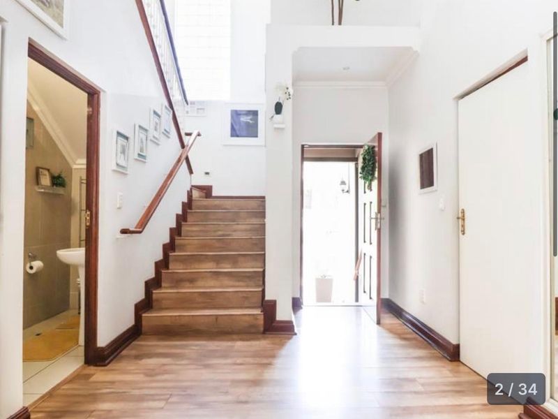 Bright and welcoming entrance hall featuring a wooden staircase, laminate flooring, and direct access to a guest bathroom.