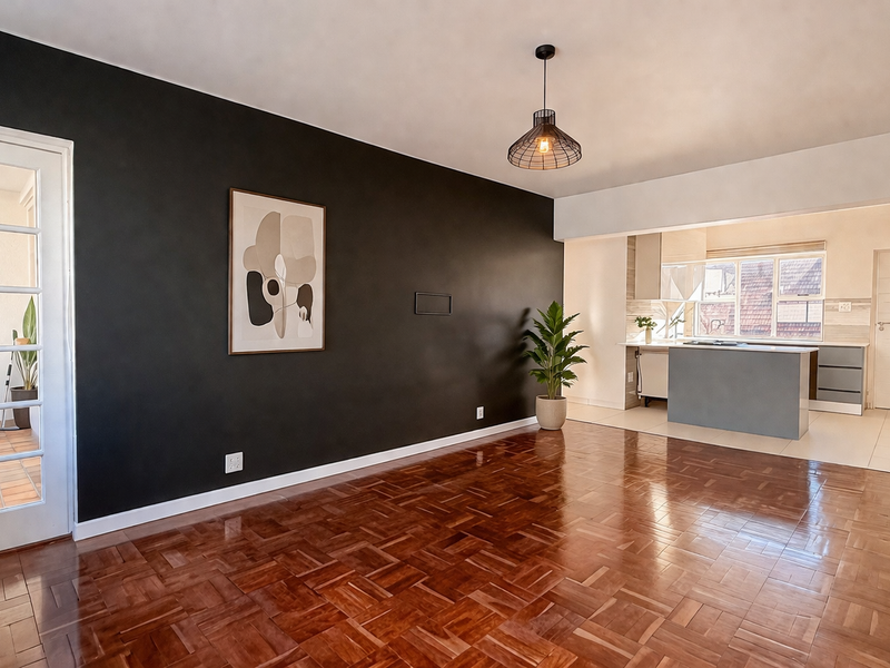 Spacious open-plan living area featuring polished parquet flooring, a modern pendant light, and a seamless transition into a functional kitchen with built-in cabinetry.