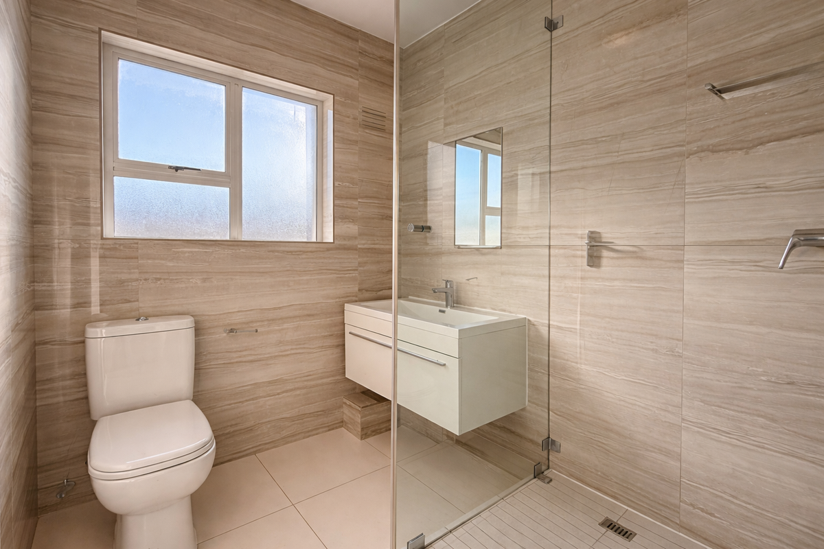 Modern bathroom featuring a walk-in shower with glass screen, wall-mounted vanity, and neutral floor-to-ceiling tiling.