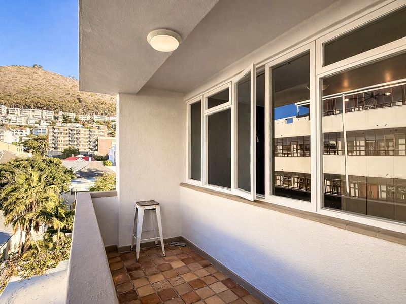 A private balcony featuring terracotta tiling, white aluminum window frames, and a concrete balustrade, offering an elevated view of the surrounding neighborhood.
