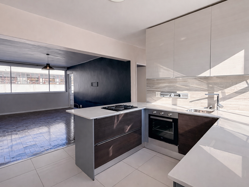 Modern open-plan kitchen featuring stone countertops, built-in oven, and gas hob, seamlessly flowing into a spacious living area with parquet flooring.