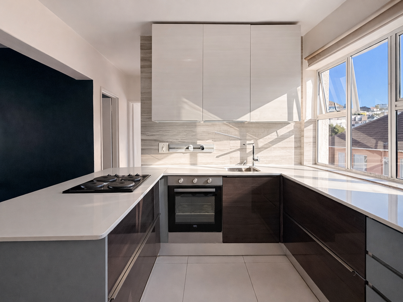 Modern kitchen featuring sleek cabinetry, stone countertops, integrated electric hob and oven, and a bright window with natural light.