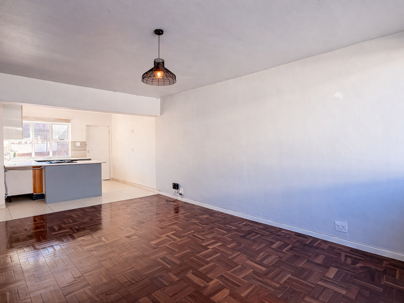 Spacious open-plan living area featuring classic parquet flooring, a functional kitchen island, and neutral walls, offering a versatile blank canvas for your interior design.