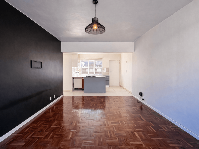Open plan living area featuring polished parquet flooring, a modern pendant light, and a functional kitchen space with island cabinetry.