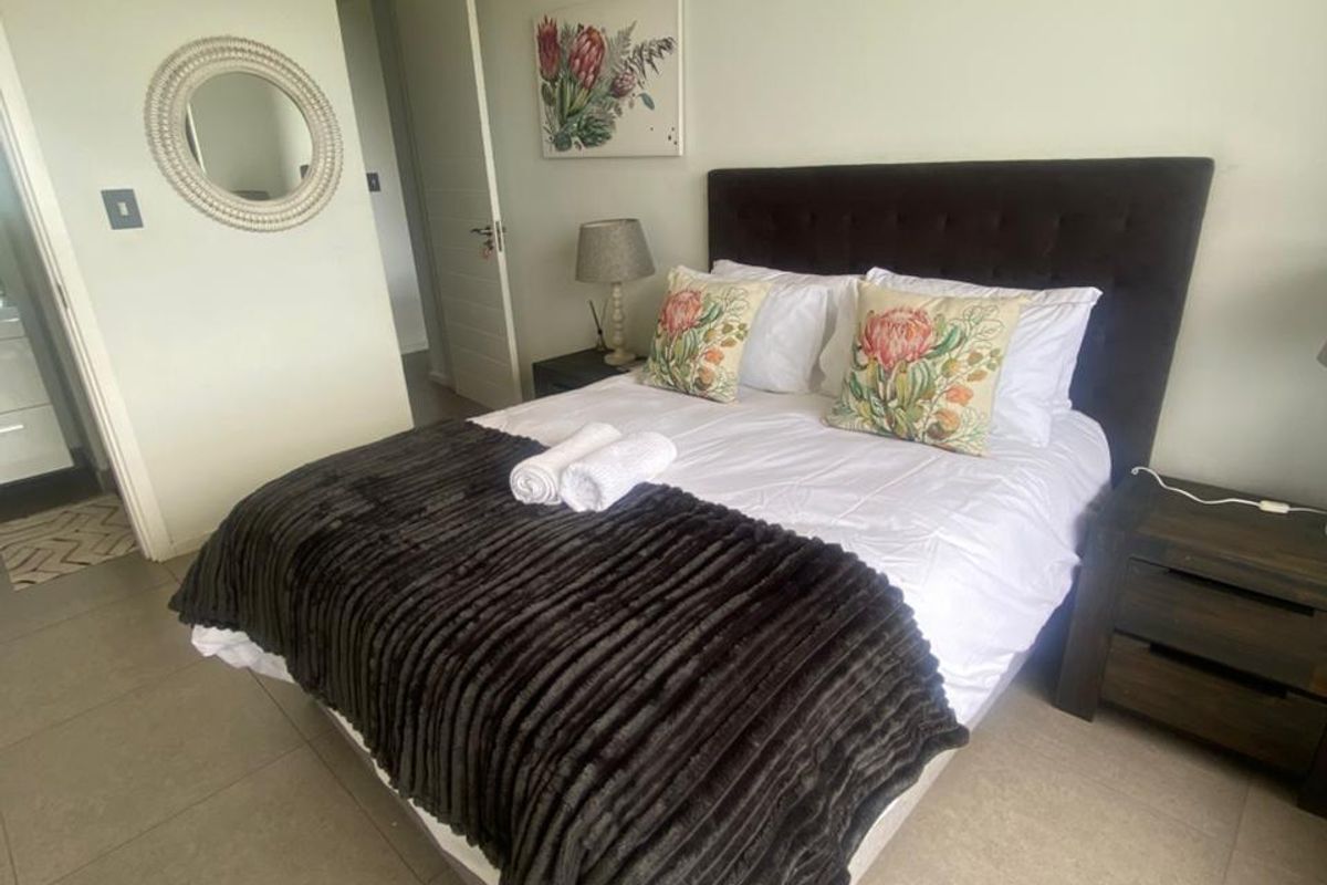 A well-maintained bedroom featuring neutral floor tiles, recessed ceiling lighting, and a wall-mounted air conditioning unit.