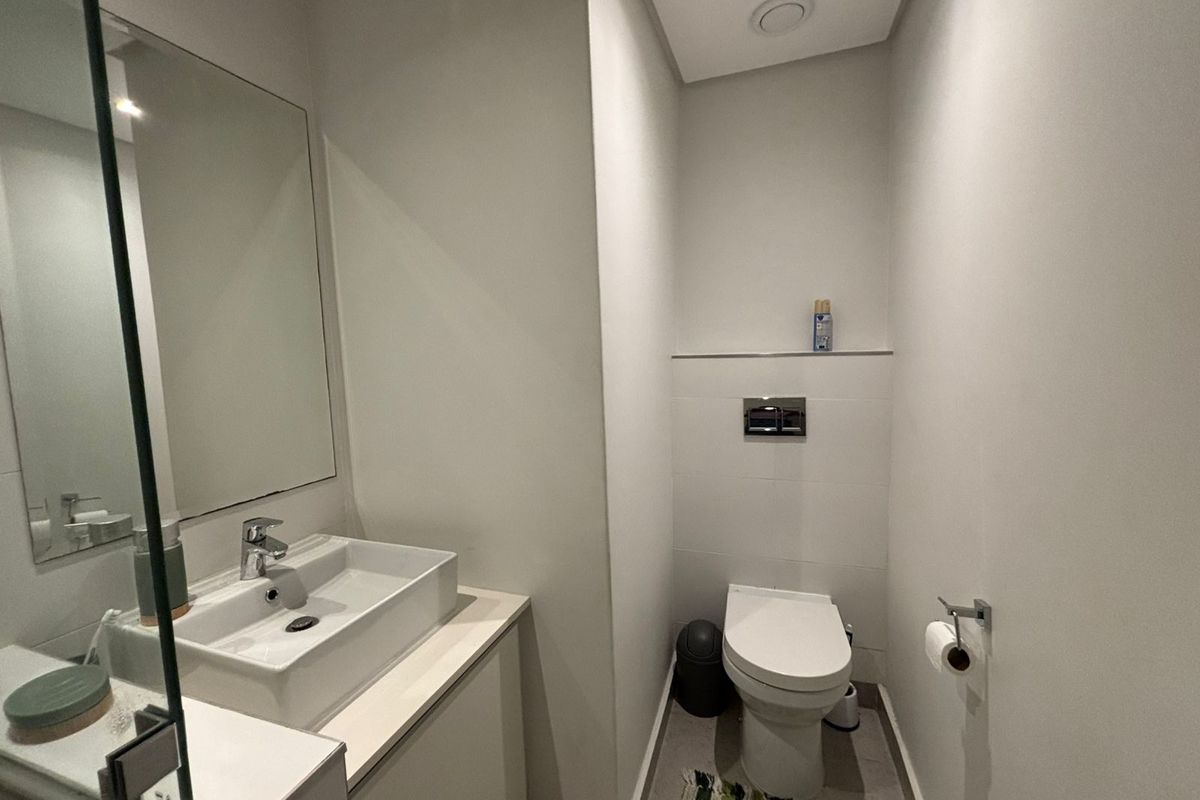 A modern guest bathroom featuring a wall-mounted toilet with a concealed cistern, a vessel sink on a vanity cabinet, and a large wall mirror.