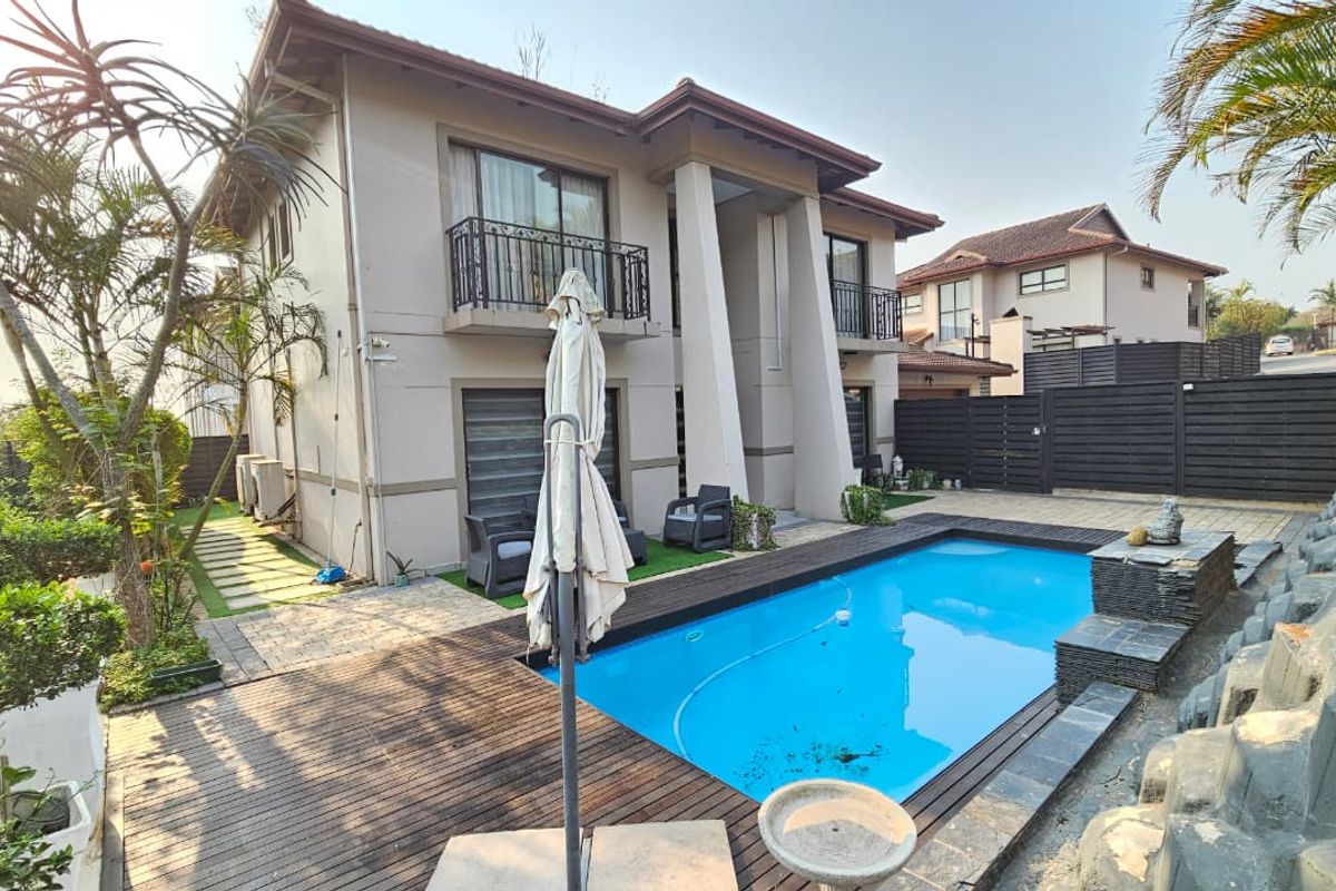 Rear view of the townhouse featuring a private swimming pool, timber decking, and a landscaped garden area with balcony access.