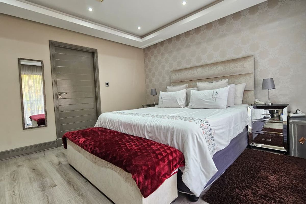 A well-maintained bedroom featuring recessed ceiling lighting, a decorative feature wall, and modern wood-look flooring.