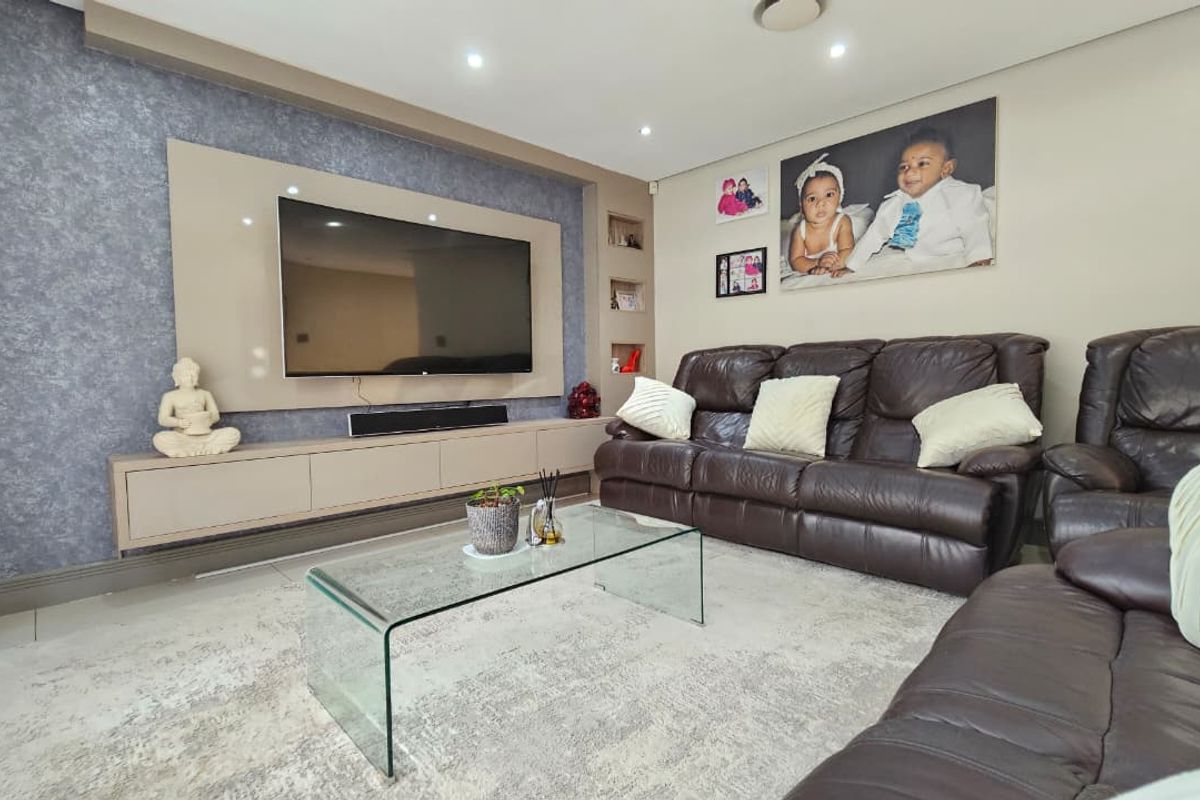 A well-maintained living room featuring a custom built-in media wall with integrated cabinetry, recessed shelving, and modern downlighting.