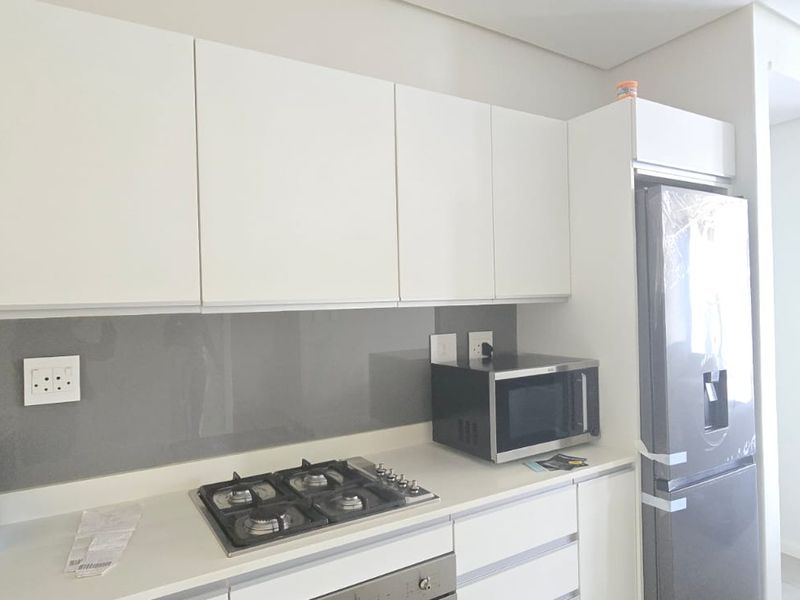 Modern kitchen featuring sleek white cabinetry, a grey glass splashback, integrated gas hob, and built-in oven with a contemporary finish.