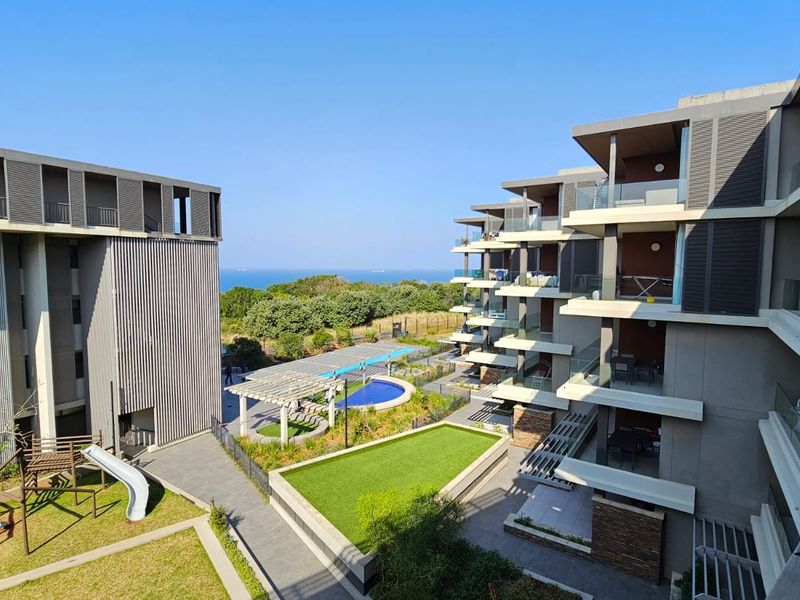 Elevated view of the apartment complex grounds, featuring landscaped gardens, a swimming pool, and modern architectural facades with private balconies.