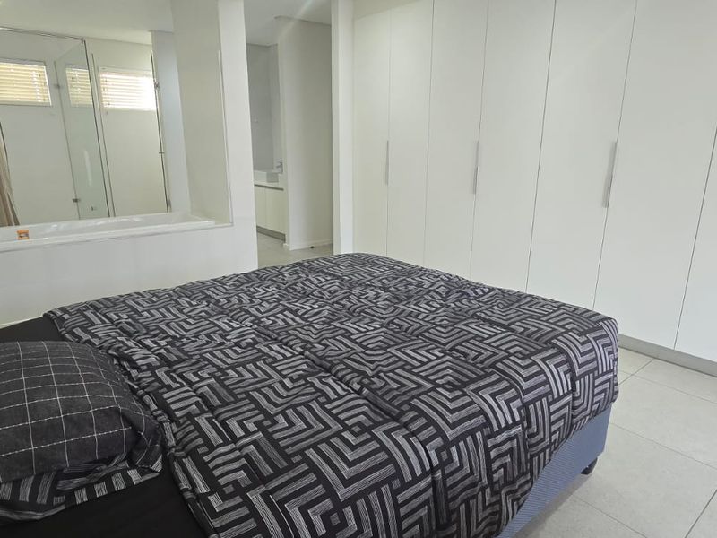 Spacious bedroom featuring extensive built-in floor-to-ceiling cabinetry and an integrated en-suite bathroom with a bathtub, finished with modern neutral tiling.