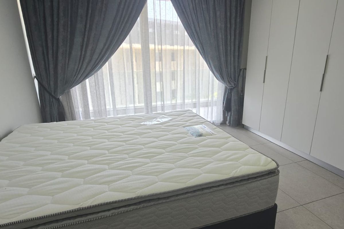 A bright bedroom featuring built-in floor-to-ceiling wardrobes, tiled flooring, and large windows with curtains, offering a clean and modern living space.