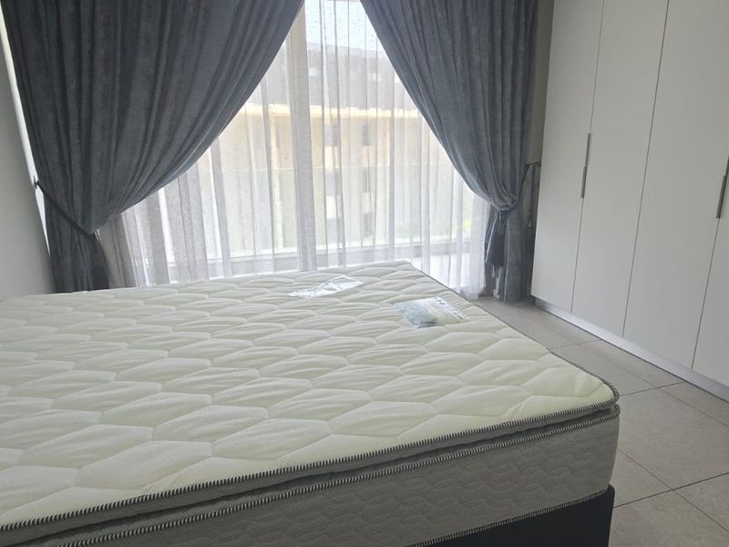 A bright bedroom featuring built-in floor-to-ceiling wardrobes, tiled flooring, and large windows with curtains, offering a clean and modern living space.