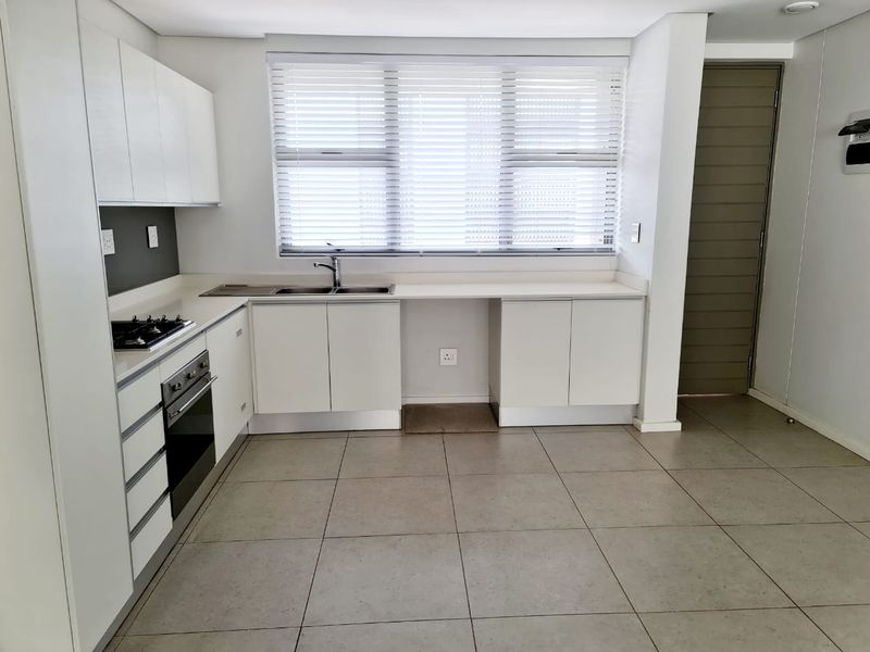 Modern kitchen featuring white cabinetry, stone countertops, integrated oven and hob, and large format floor tiles with ample natural light.