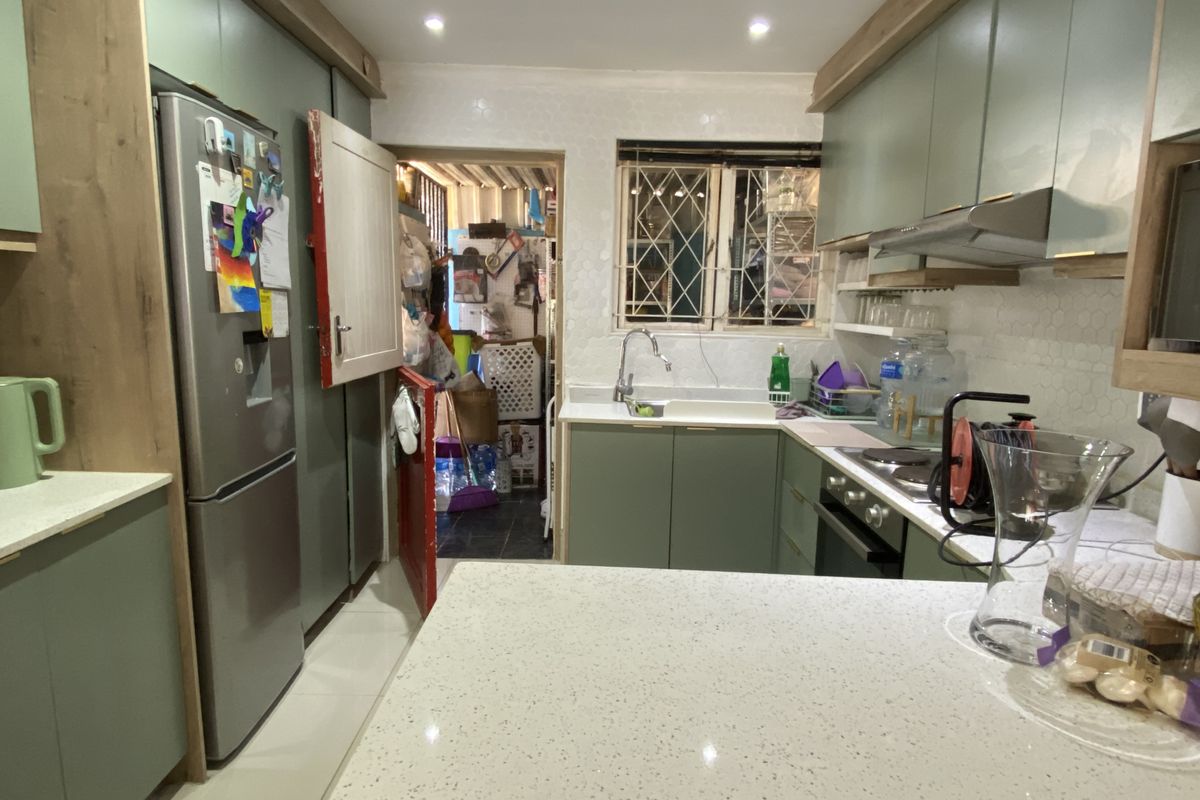Modern kitchen featuring sage green cabinetry, stone countertops, built-in oven, extractor fan, and a tiled backsplash, with an adjacent utility area.