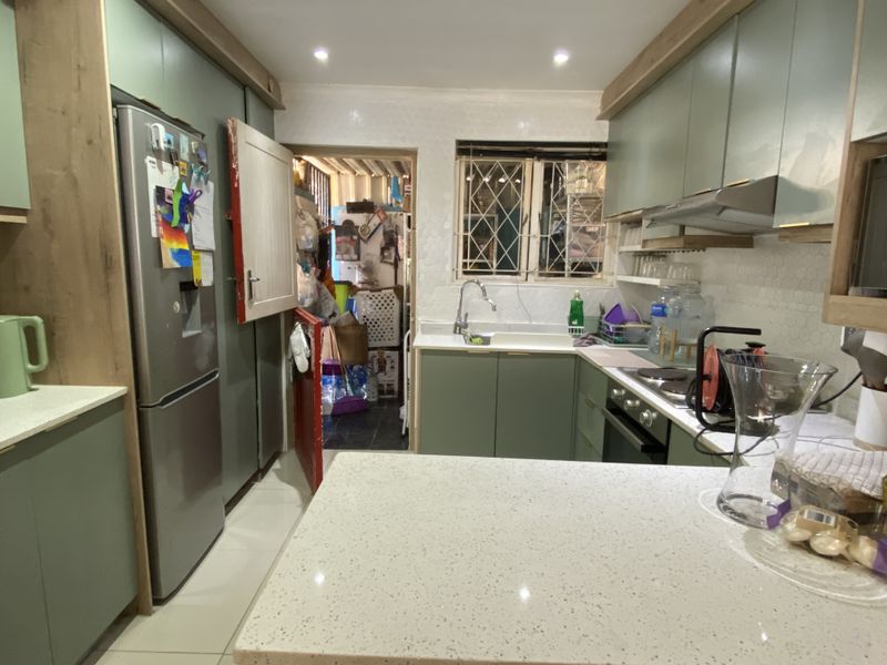 Modern kitchen featuring sage green cabinetry, stone countertops, built-in oven, extractor fan, and a tiled backsplash, with an adjacent utility area.