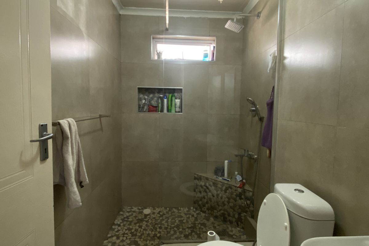 A bathroom featuring a walk-in shower with pebble flooring, wall-mounted shower head, built-in wall niche, and a standard toilet.