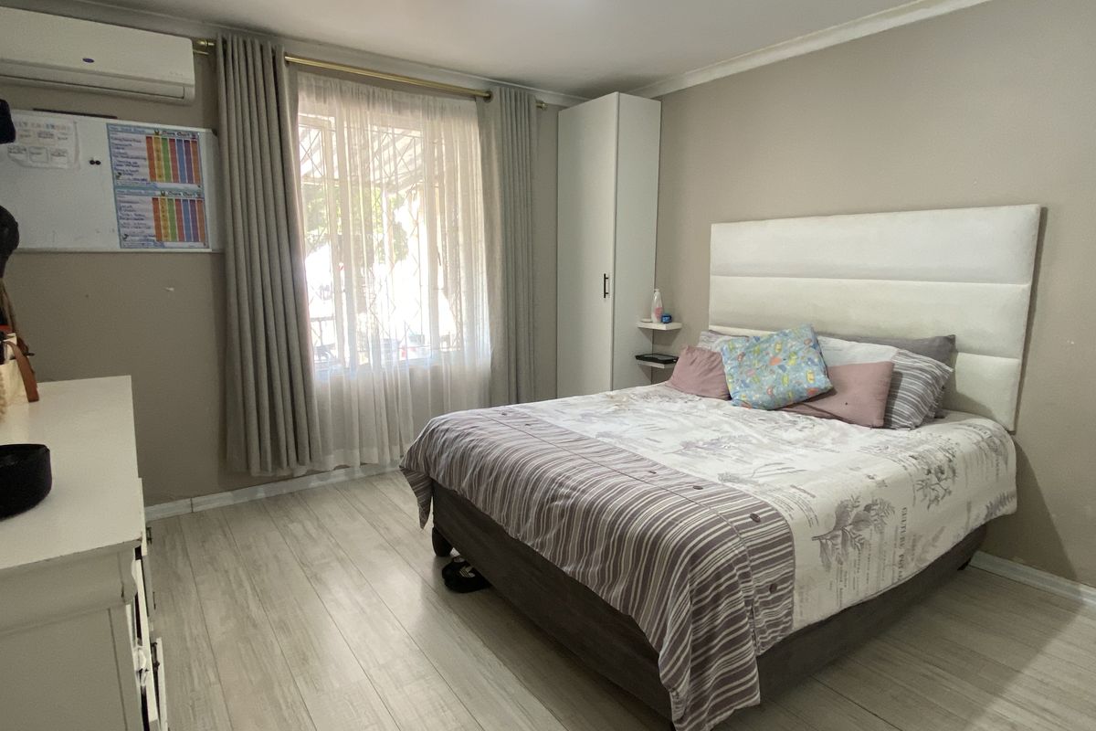 A well-lit bedroom featuring light-toned wood-look flooring, a built-in wardrobe, and a wall-mounted air conditioning unit.