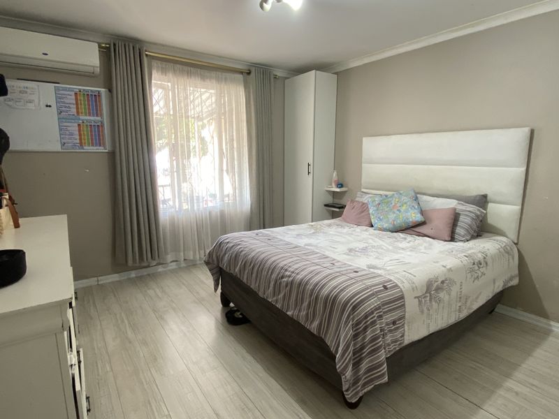 A well-lit bedroom featuring light-toned wood-look flooring, a built-in wardrobe, and a wall-mounted air conditioning unit.
