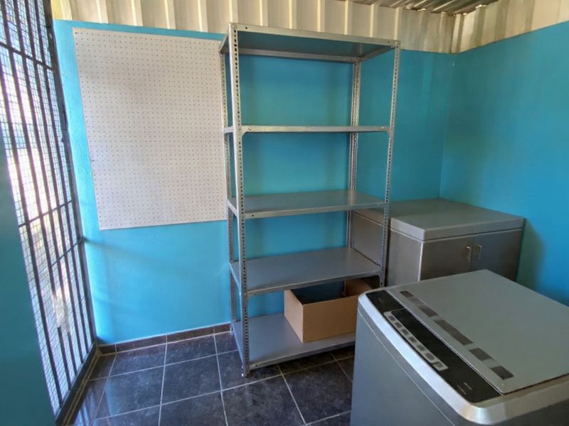 A utility space featuring tiled flooring, blue painted walls, and a metal security gate, suitable for storage or laundry purposes.