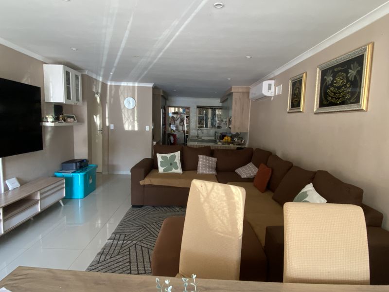 Open plan living area featuring tiled flooring, recessed ceiling lighting, and a wall-mounted air conditioning unit, flowing into a compact kitchen space.