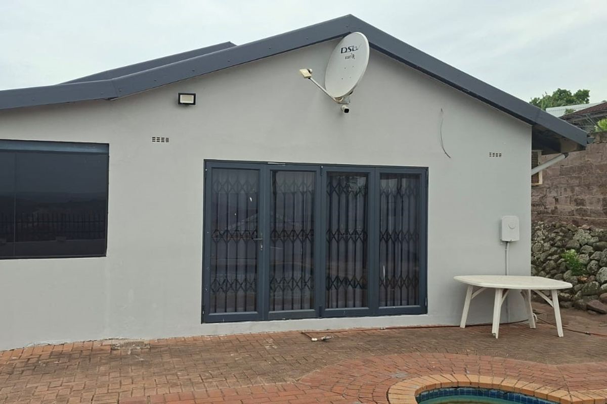 Rear exterior view of the property featuring a paved patio area, swimming pool edge, and secure sliding glass doors with security gates.