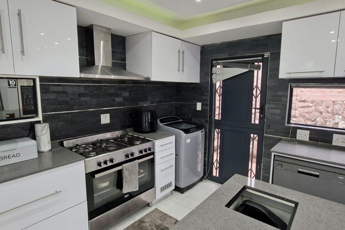 Modern kitchen featuring high-gloss white cabinetry, dark stone countertops, a gas stove with extractor fan, and integrated appliance space.