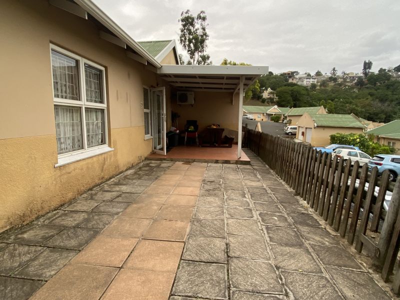 A paved outdoor patio area with a covered section, featuring a wooden fence boundary and views of the surrounding townhouse complex.