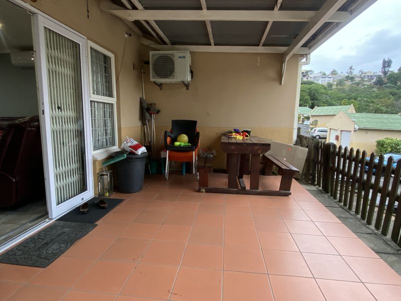 A covered patio area featuring tiled flooring, a wall-mounted air conditioning unit, and direct access to the interior living space via sliding doors.