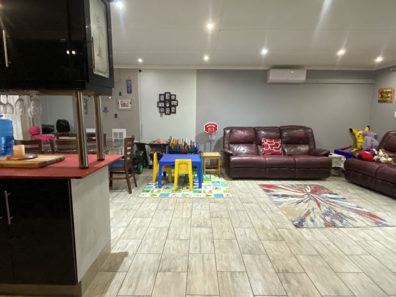 Open plan living area featuring wood-look tiled flooring, recessed downlighting, and a wall-mounted air conditioning unit.
