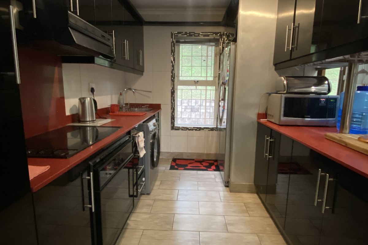 Galley-style kitchen featuring high-gloss black cabinetry, contrasting red countertops, integrated hob, extractor fan, and tiled flooring with a window for natural light.