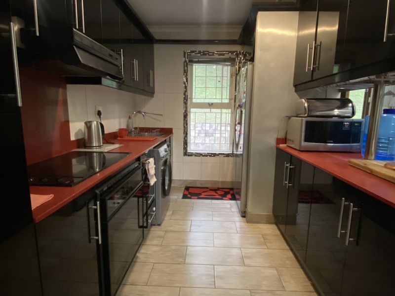 Galley-style kitchen featuring high-gloss black cabinetry, contrasting red countertops, integrated hob, extractor fan, and tiled flooring with a window for natural light.