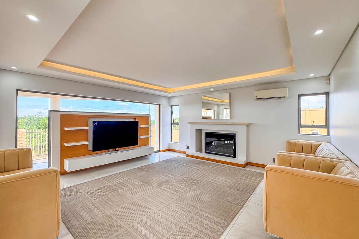 Spacious living room featuring a modern built-in fireplace, recessed tray ceiling with ambient lighting, and large sliding doors opening to an outdoor balcony.